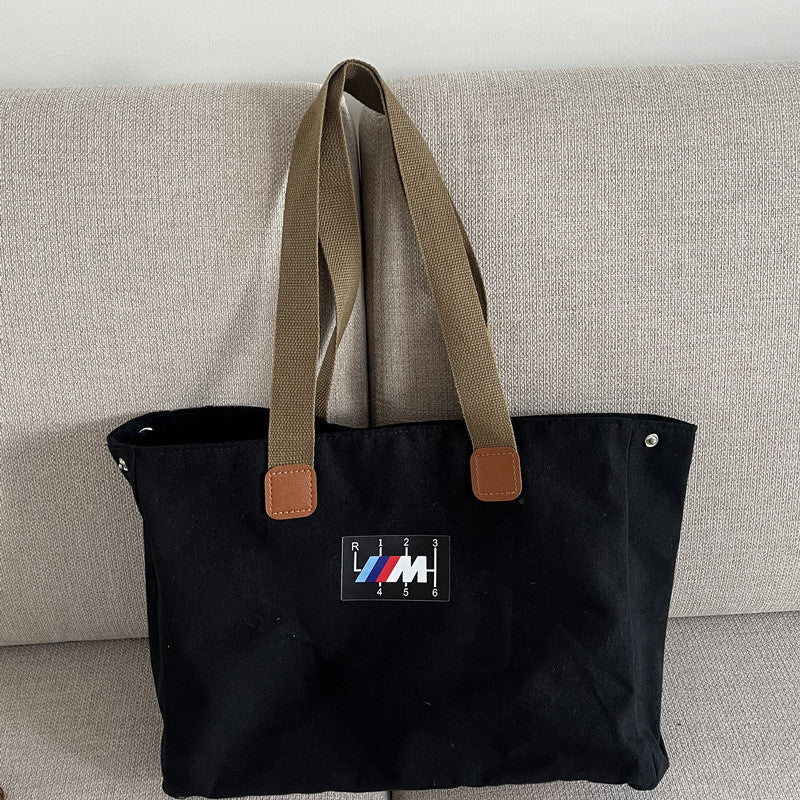 BMW canvas tote bag black with M stripe patch on couch